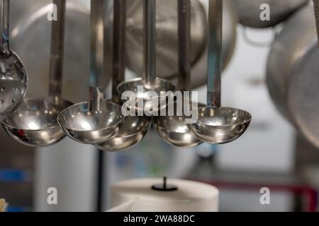 Stainless steel cooking utensils hanging in a commercial industrial kitchen. Stock Photo