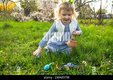 easter eggs hunt. Little girl with baskets in hands gathering colorful egg in park Stock Photo