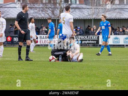 Macclesfield FC player sits on the ground and is seen by the female physio after hurting his nose in a tackle Stock Photo