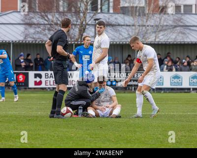 Macclesfield FC player sits on the ground and is seen by the female physio after hurting his nose in a tackle Stock Photo