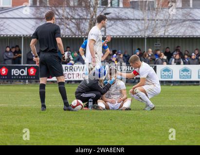 Macclesfield FC player sits on the ground and is seen by the female physio after hurting his nose in a tackle Stock Photo
