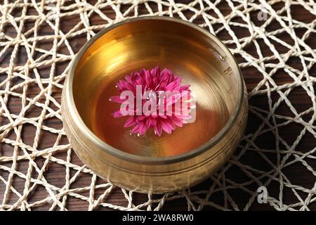 Tibetan singing bowl with water and beautiful flower on wooden table Stock Photo