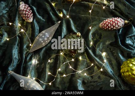 Christmas tree toys and light garland lying on dark green velvet background. Christmas decorations close up photo. Stock Photo