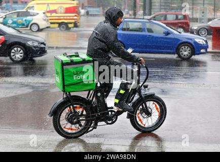 An Uber Eats delivery driver rides an e-bike across a road in heavy rain, Berlin, 23 06 2023 Stock Photo