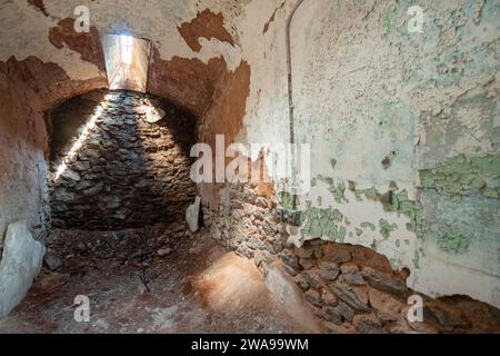 A cell with a rubble floor and rough stone back wall is lit by a narrow skylight shaft at Eastern State Penitentiary, Philadelphia, Pennsylvania. Stock Photo