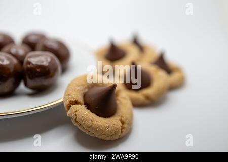 Macro defocused view of round chocolate candies on a small white porcelain plate, surrounded by home made peanut butter cookies with a chocolate drop Stock Photo