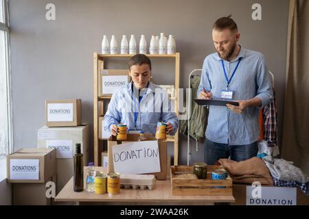 Two people working in charitable foundation. Happy volunteer at workplace with donation food box. Volunteers sort donations during food drive Stock Photo