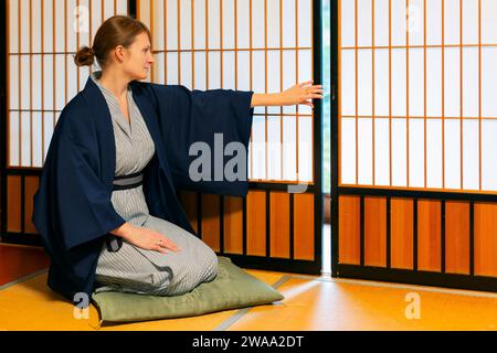 Traditional japanese house or ryokan with gaijin caucasian woman in kimono and tabi socks opening shoji sliding paper doors sitting on tatami mat floo Stock Photo