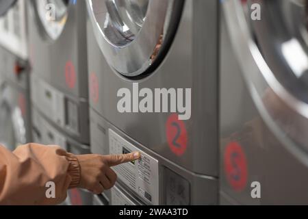 Female hand visible pushing a button on the machine at a laundromat. Automatically controlled laundry machine with a touch of a button Stock Photo