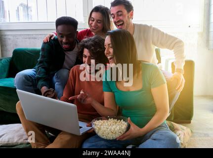 Happy best friends using modern laptop computer together. Cheerful positive young multiethnic women enjoying funny TV show, laughing, discussing favor Stock Photo