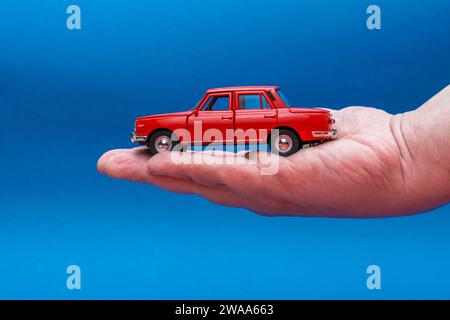 Hand holding red toy car isolated on blue background Stock Photo