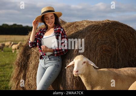 Smiling farmer with tablet and sheep near hay bale on farm Stock Photo