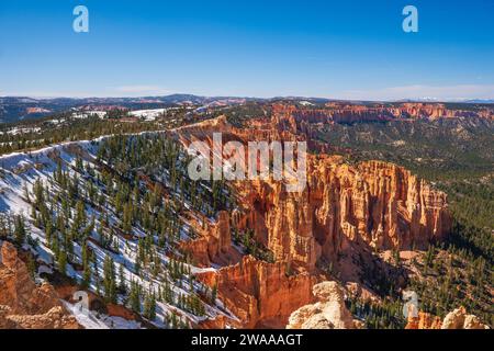 Panorama over Bryce Canyon from a high viewpoint, snow remaining on the ground, clear blue sky, forest, hoodoos. Stock Photo