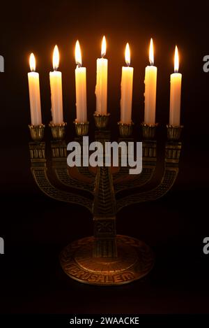 Menorah with the word JERUSALEM written on its base with 7 lit candles isolated on a dark background. Stock Photo