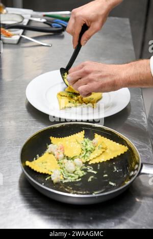 High angle of anonymous man putting delicious ravioli pasta with cucumber and shrimps on plate while working in restaurant kitchen Stock Photo