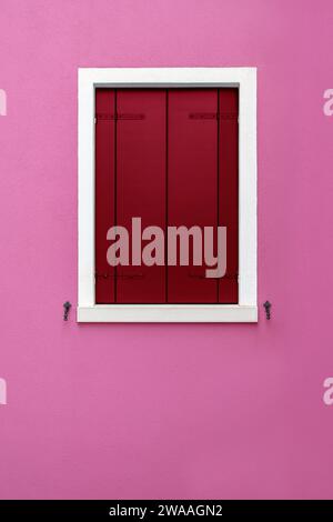 Decorated red smooth closed wooden window shutter with white frame on colorful pink wall background Stock Photo
