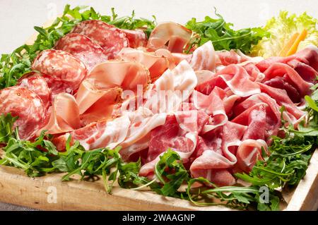 Closeup high angle of assorted fresh lettuce with delicious mixed Italian prosciutto hams and salami placed on wooden tray Stock Photo