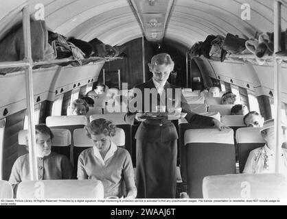 Airline travelling in the 1950s. A group of women and  men on an swedish passenger airplane in the 1950s. The female flight attendant is standing in the middle of the airplane serving coffee and sandwiches to the passengers. Sweden 1957 Stock Photo