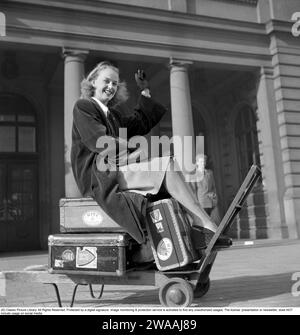 In the 1940s. A young woman photographed sitting on her luggage,  suitcases on each other on a railway trolley, waiting for a taxi to go further. 1948. Conard ref 917 Stock Photo