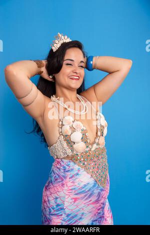 Beautiful woman, wearing a tiara and seashell bracelets, against a blue background, touching her black hair. Yemanja worshiper. Stock Photo