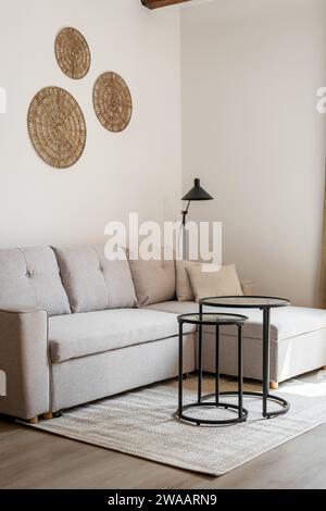 Vertical shot of a beige style corner sofa stands on the floor with a coffee table and circle wall decor and a floor lamp. Concept of a modern living Stock Photo