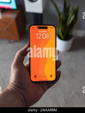 LONDON - NOVEMBER 05, 2023: Apple iPhone 14 Pro held in hand with bright orange color wallpaper on screen Stock Photo