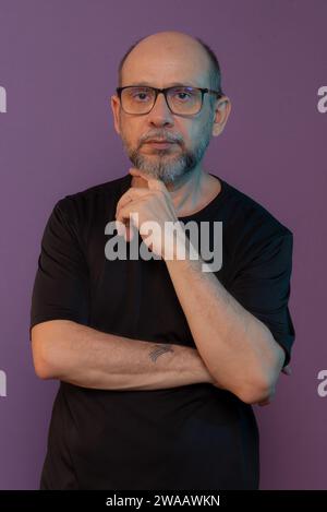 Bearded, bald white man wearing prescription glasses wearing black clothing looking at the camera posing for a photo. Isolated on dark lilac backgroun Stock Photo