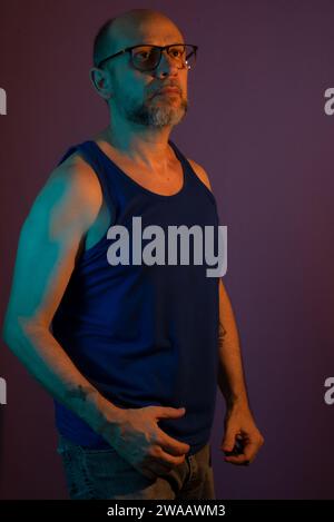 Portrait of bearded, bald man wearing prescription glasses with blue shirt. Isolated on dark lilac background. Stock Photo