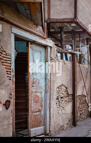 Old wooden door with peeling paint, opening onto a staircase leading to a dilapidated house in Kala, Tbilisi Old town, Georgia Stock Photo