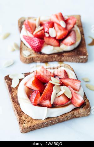 Crispy breakfast toasts with ricotta, strawberries and almonds on a white marble background. Stock Photo
