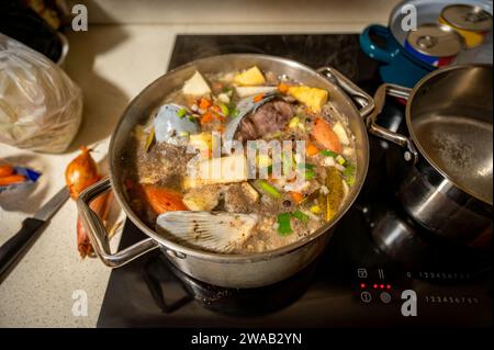 Cooking of fish soup in pot on ceramic hob, closeup. Christmas fish soup. Stock Photo