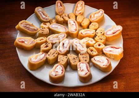 Sliced piece of cheese roulade with filling (ham, soft cheese, flax seed) on white plate on wooden table, closeup. Stock Photo