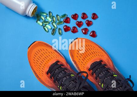 Scattered yellow Omega 3 capsules from a jar and red decorative hearts and orange running sneakers on a blue background Stock Photo