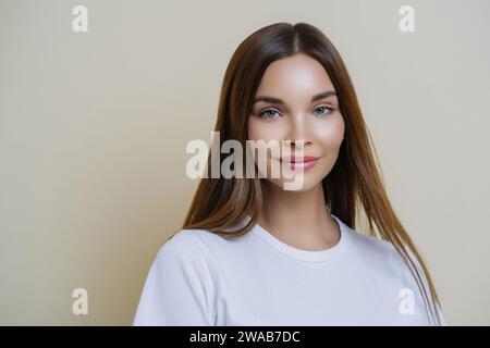 Portrait of a confident young woman in a white t-shirt, with long brown hair, and a natural makeup look Stock Photo