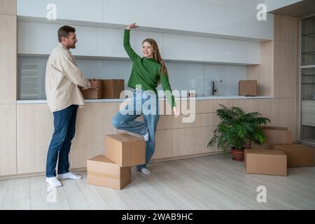 Happy young family couple moving to new apartment with modern interior, kitchen. Stock Photo
