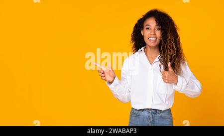 Excited African American Gesturing Thumbs Up Woman Pointing Aside, Studio Stock Photo