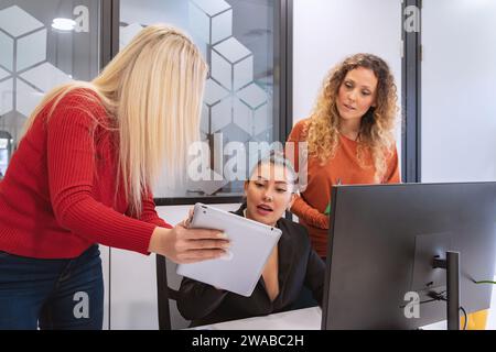 Three business professionals using a tablet and a desktop computer to discuss work in a corporate office setting. Stock Photo