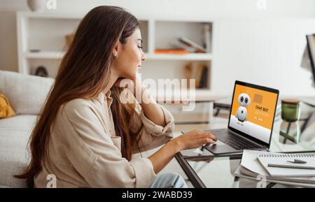 Millennial woman working at home office, using chatbot on laptop Stock Photo