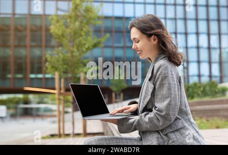 Young businesswoman browsing web on laptop sitting outdoors, side view Stock Photo