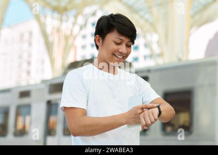 Smiling chinese man looking at watch standing on city street Stock Photo