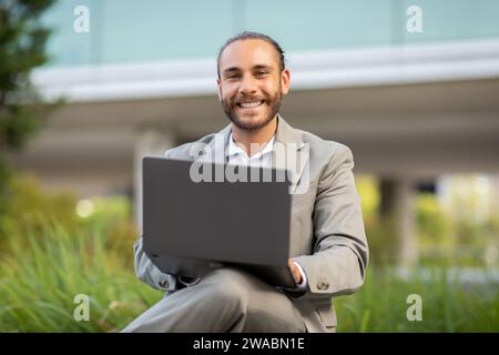 Portrait of relaxed young businessman using laptop in urban park Stock Photo