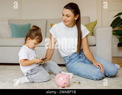 Children And Money Management. Little girl counting coins from piggybank, using calculator Stock Photo