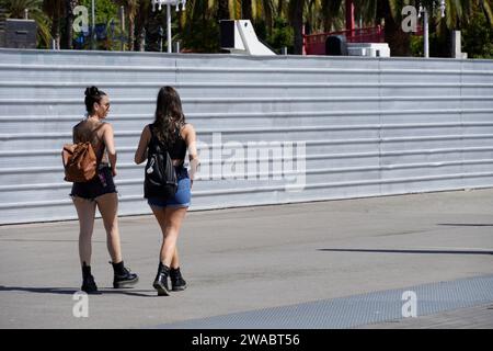 Barcelona, Spain - May 26, 2022: Two stylish young girls walk through the construction zone dressed in jean shorts and military boots, both carrying b Stock Photo