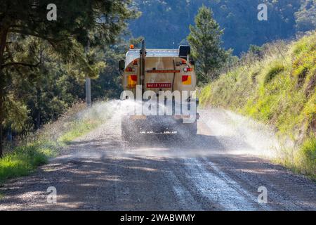 Photograph of a large water tanker spraying water on a dirt road that is under repair running through a forest to reduce dust in the Blue Mountains Stock Photo