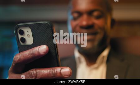 Blurred focus african american businessman holding smartphone browsing social network writing email message happy man chatting remotely communicating Stock Photo