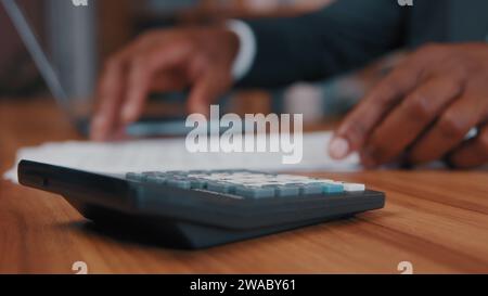 Close-up african american man calculates salary enters data in laptop accountant businessman makes calculation looks for information in paper Stock Photo