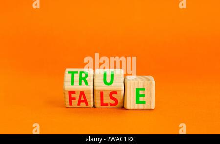 False or true symbol. Turned wooden cubes and changed the word false to true or vice versa. Beautiful orange table, orange background, copy space. Bus Stock Photo