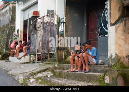People resting near the road in an unusual Asian village. Children are playing and adults are talking sitting on the roadside. Bali, Indonesia - 12.09 Stock Photo