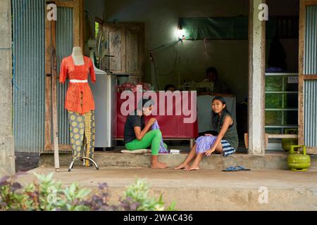 People resting near the road in an unusual Asian village. Children are playing and adults are talking sitting on the roadside. Bali, Indonesia - 12.24 Stock Photo