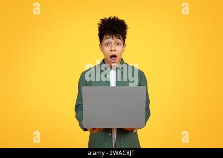 Amazed young black guy using laptop on yellow background Stock Photo